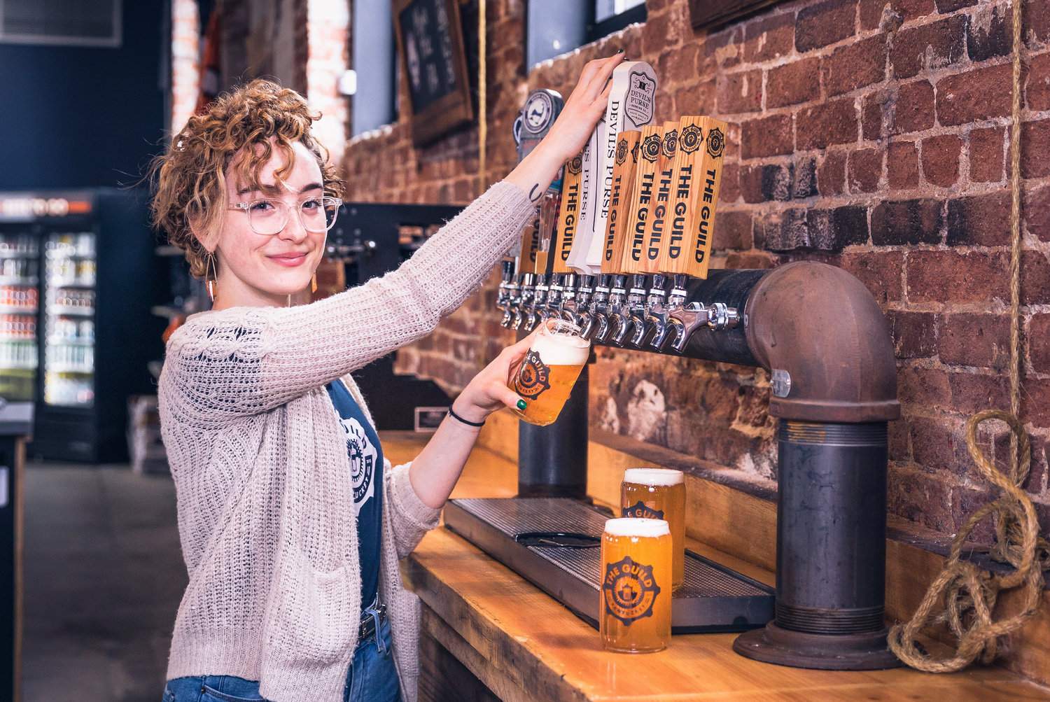 Bartender Gabrielle McCauley pours a pint of one of The Guild’s eight craft beers brewed onsite in Pawtucket